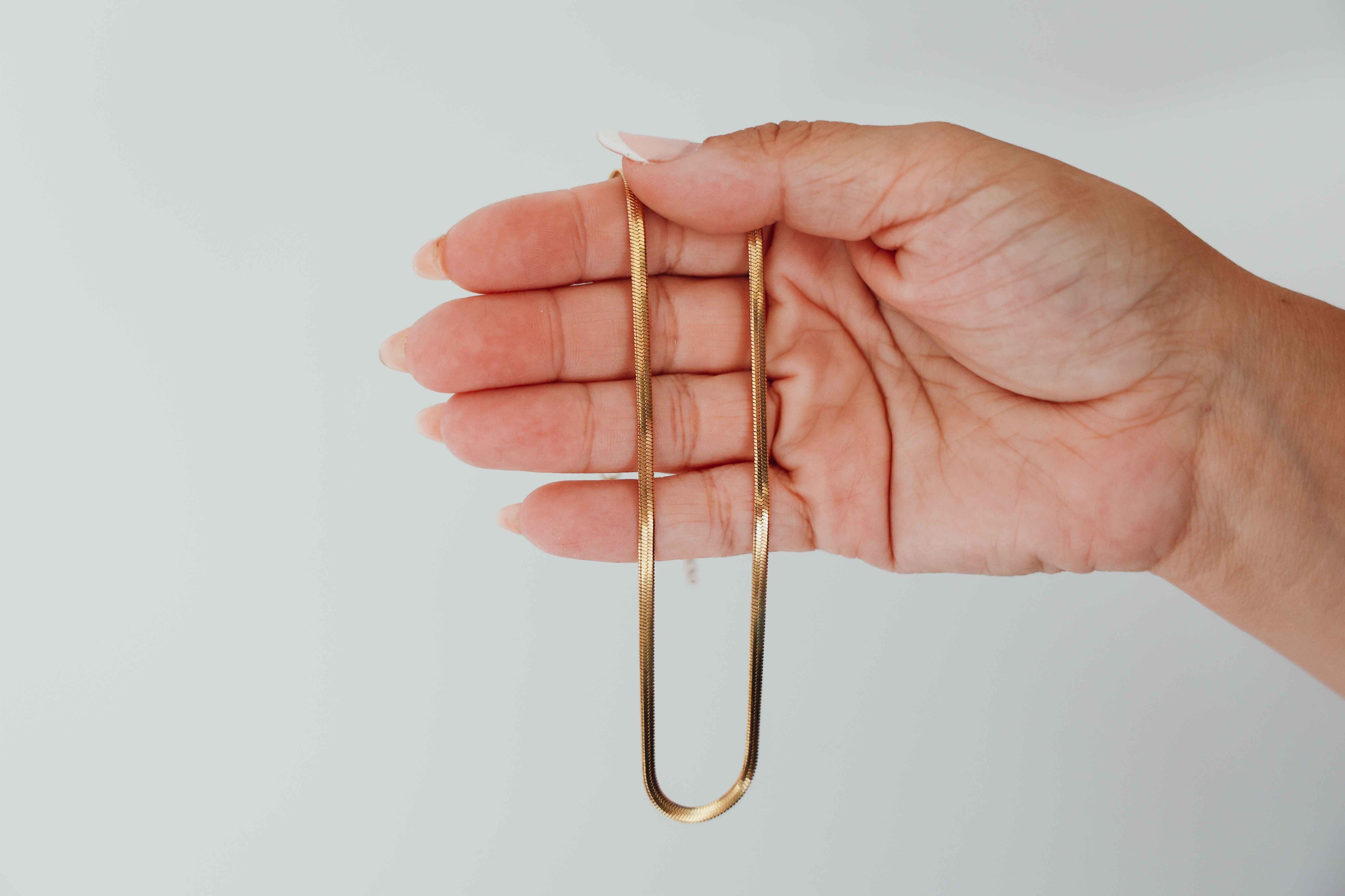 Hand holding a gold snake chain necklace against a plain background