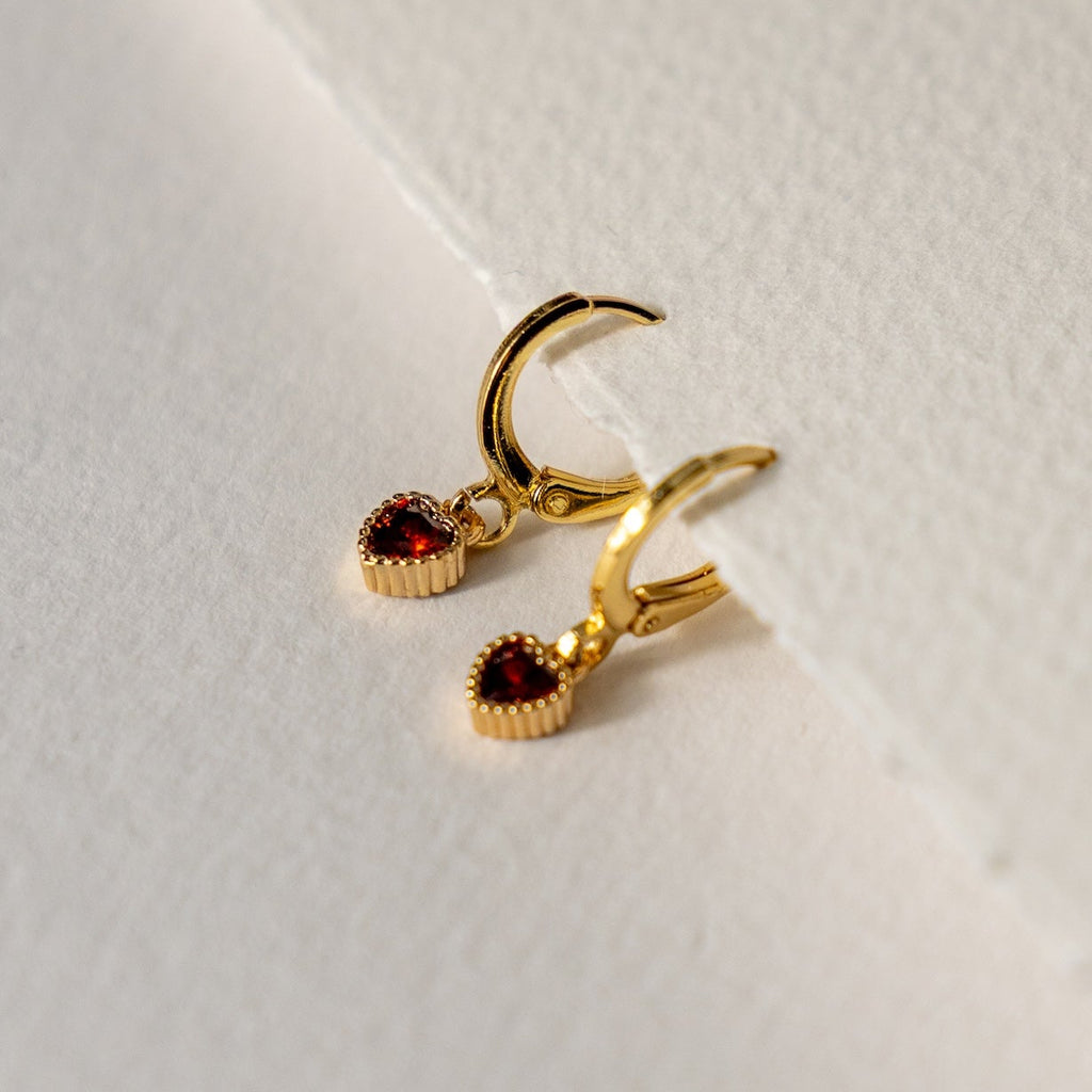 Gold hoop earrings with red gemstones on a light background