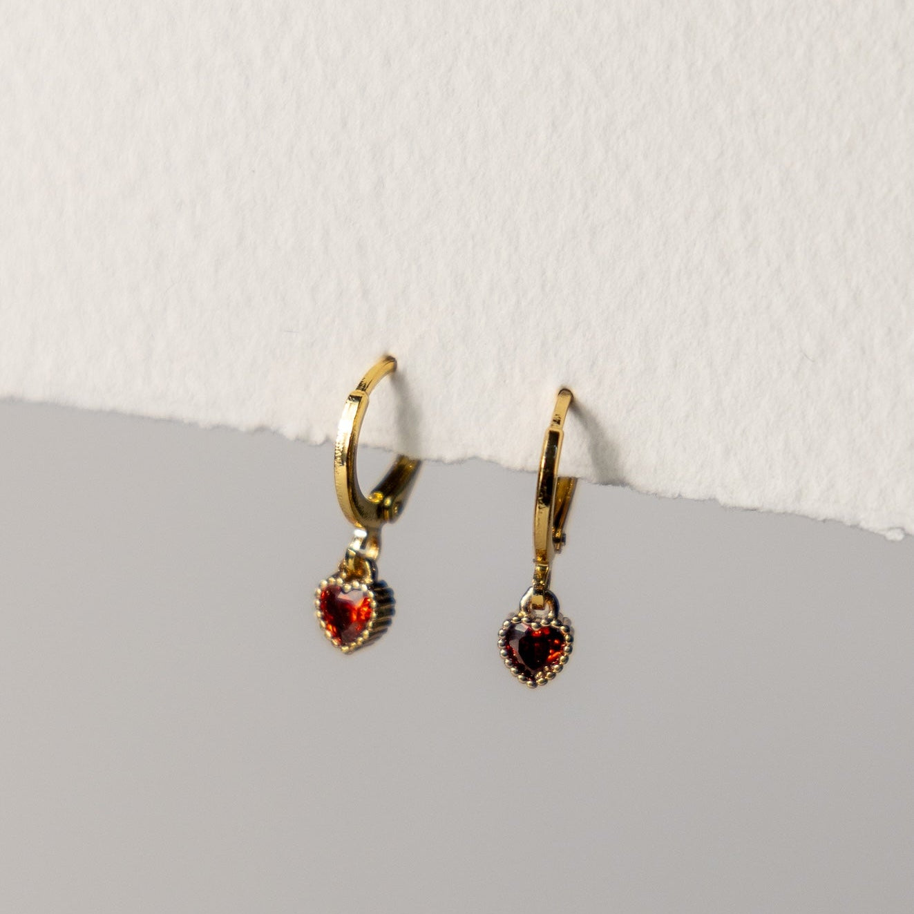 Pair of gold hoop earrings with red gemstones on a light gray surface.