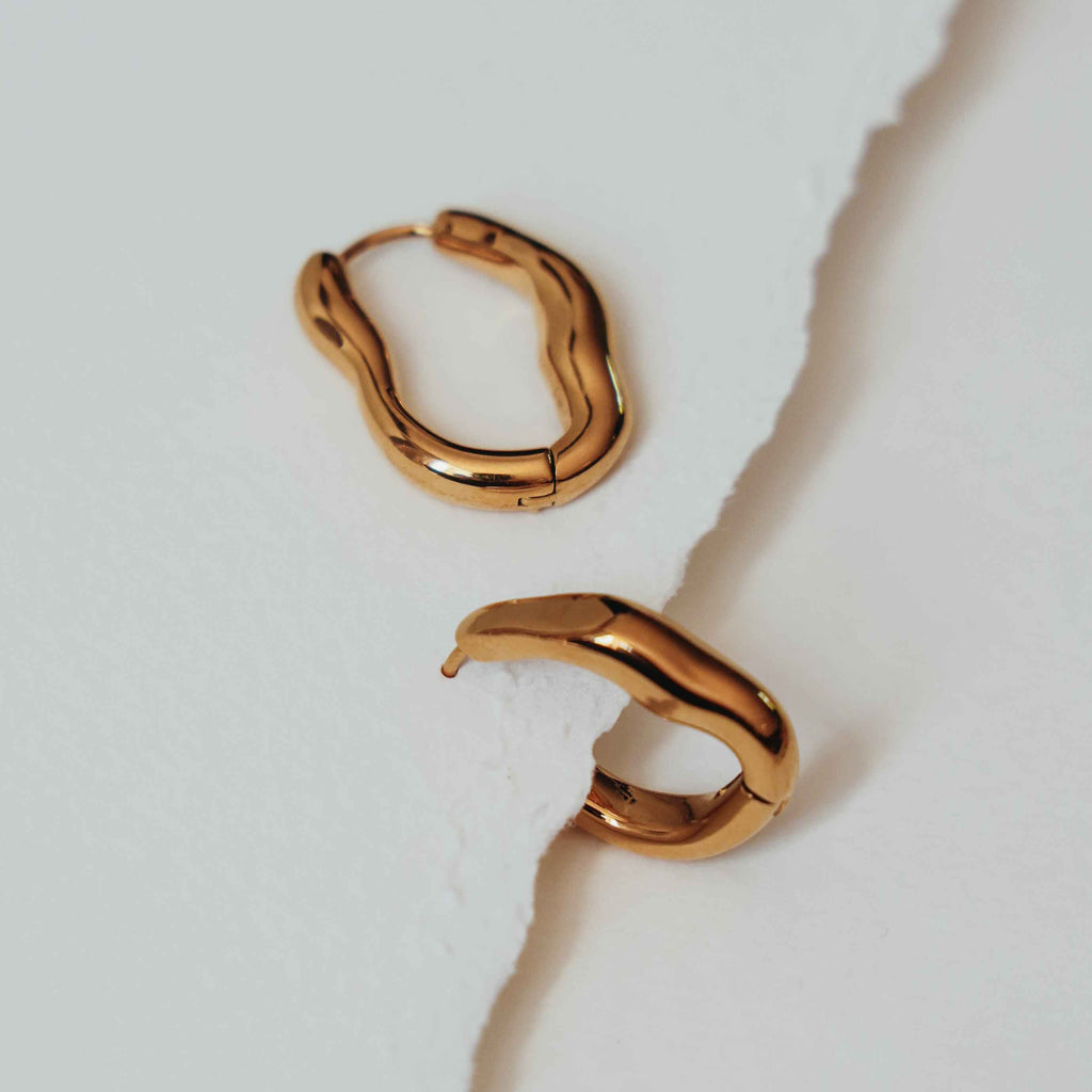 Alice wavy gold hoop earrings on a light grey background