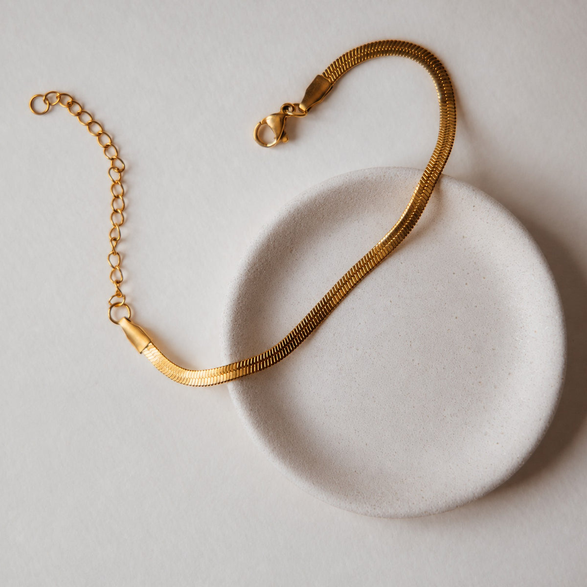 Ava gold herringbone chain bracelet from the Herringbone set, on a white dish