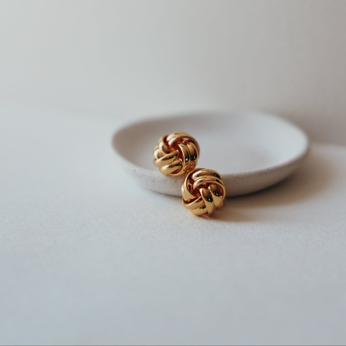 Beatrice 18k gold knot stud earrings resting on a small white dish