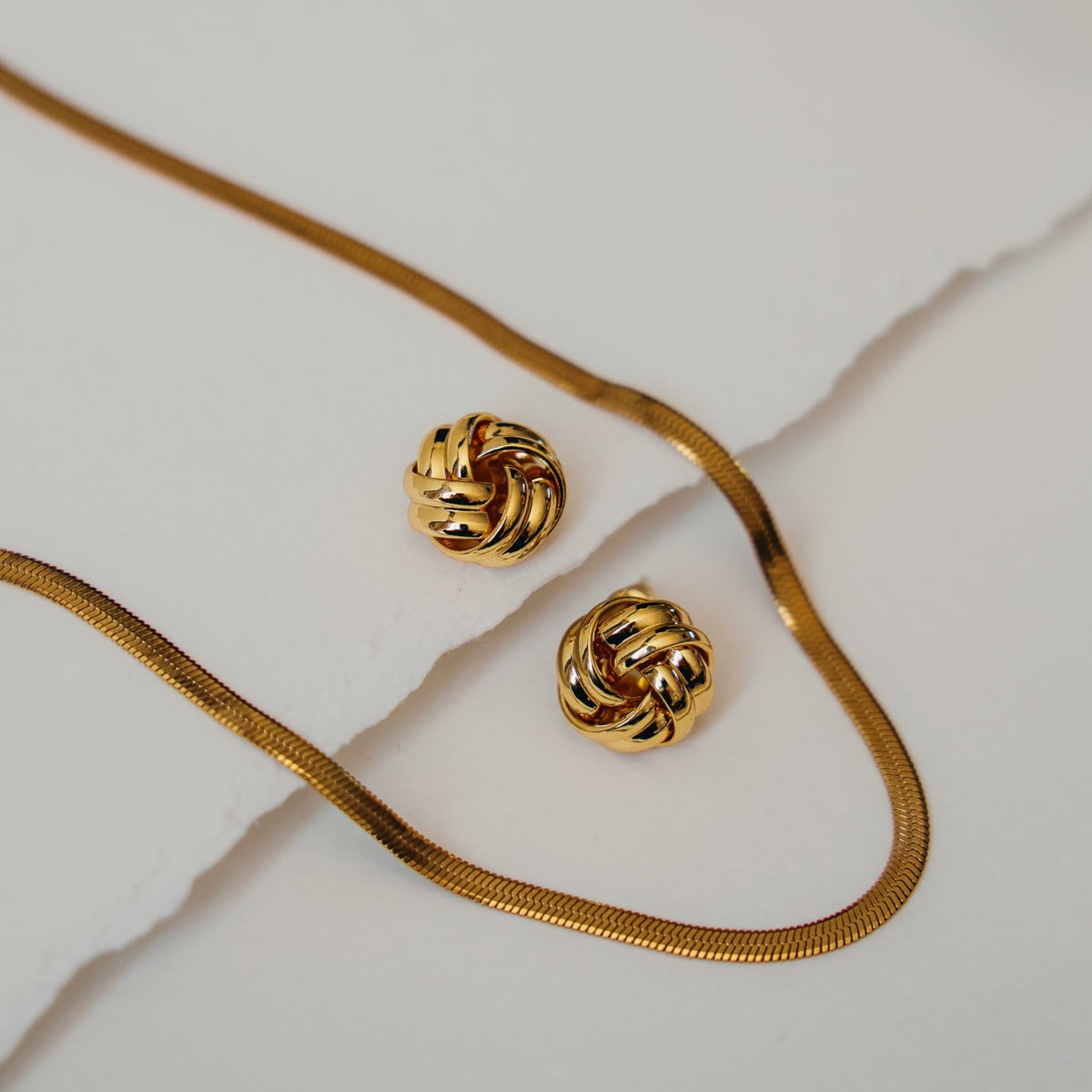 Beatrice knot stud earrings next to a gold herringbone chain