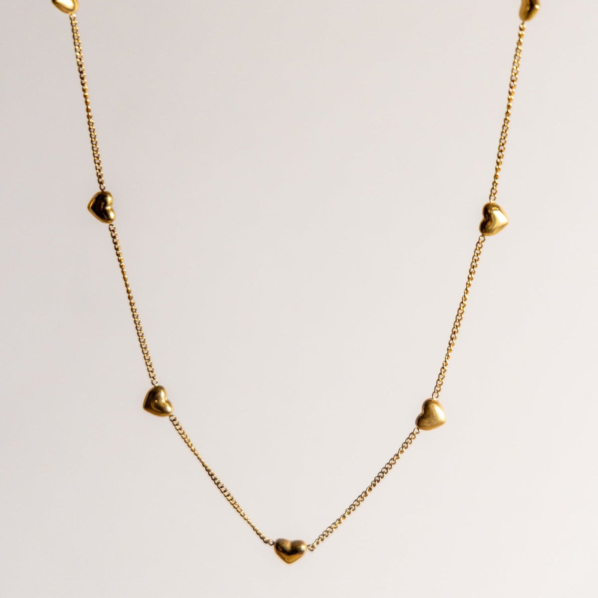 Lois gold heart necklace on a light grey background