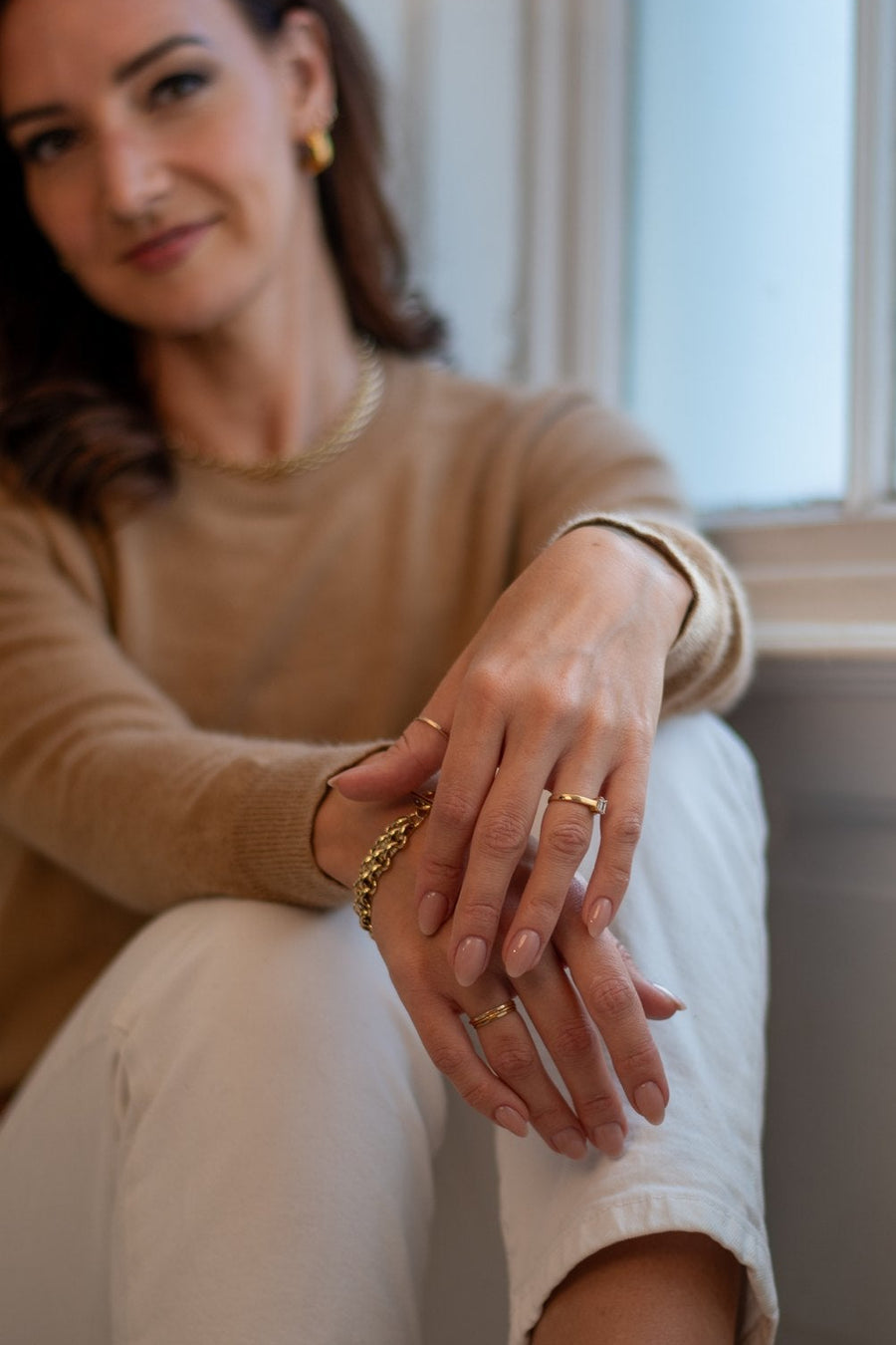Close-up of Lizz's hands wearing gold rings and a chain bracelet