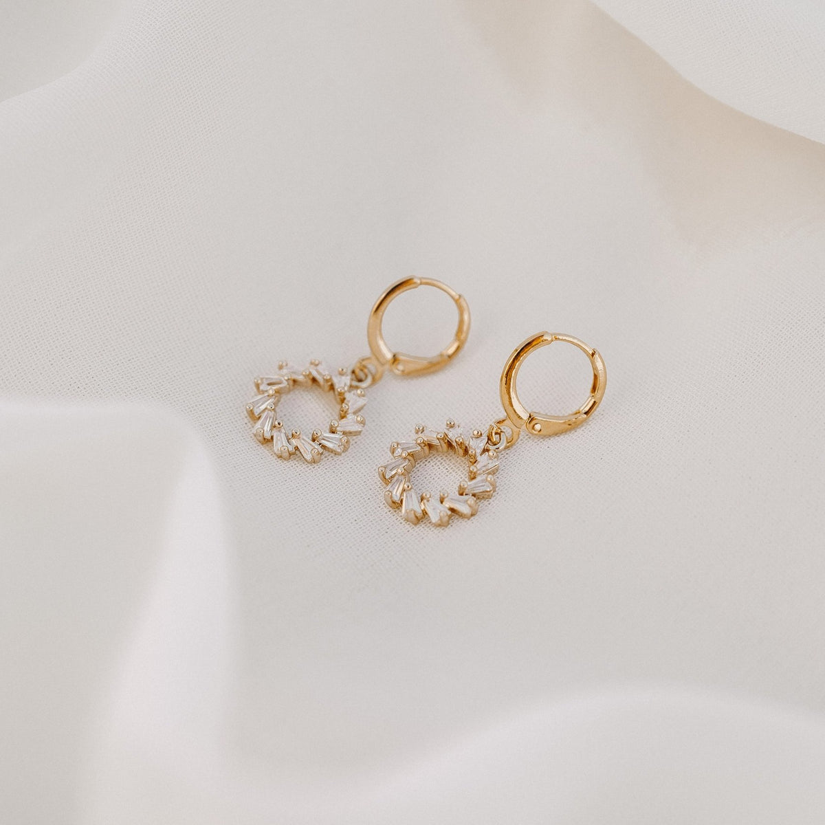 Lucy gold huggie earrings with a small circle of clear stones, on white silk