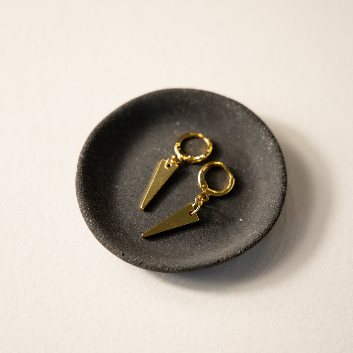 Maisie triangle drop earrings on a dark dish