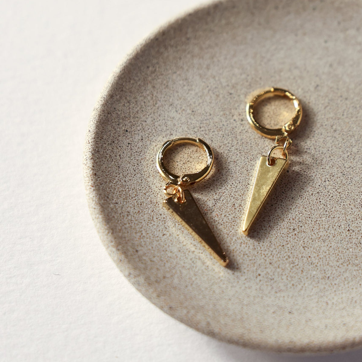 Maisie gold huggie earrings with slim triangle drops, on a stone dish