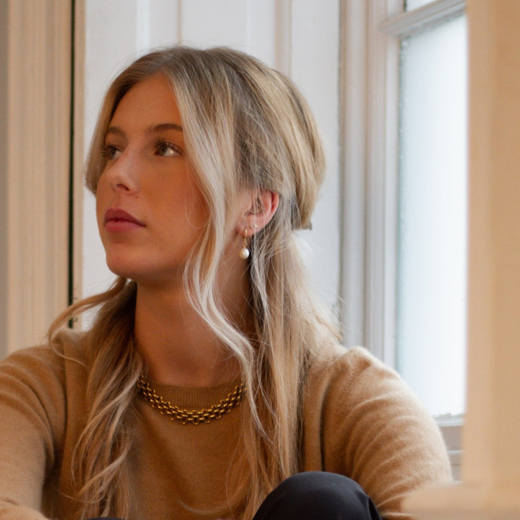 Woman in a camel jumper sitting in a window, wearing the Molly freshwater pearl earrings