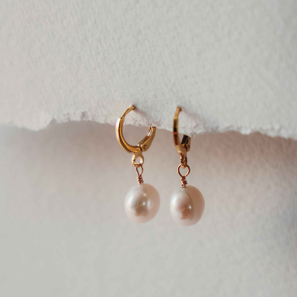 Molly gold hoop earrings with freshwater pearl drops on a light background