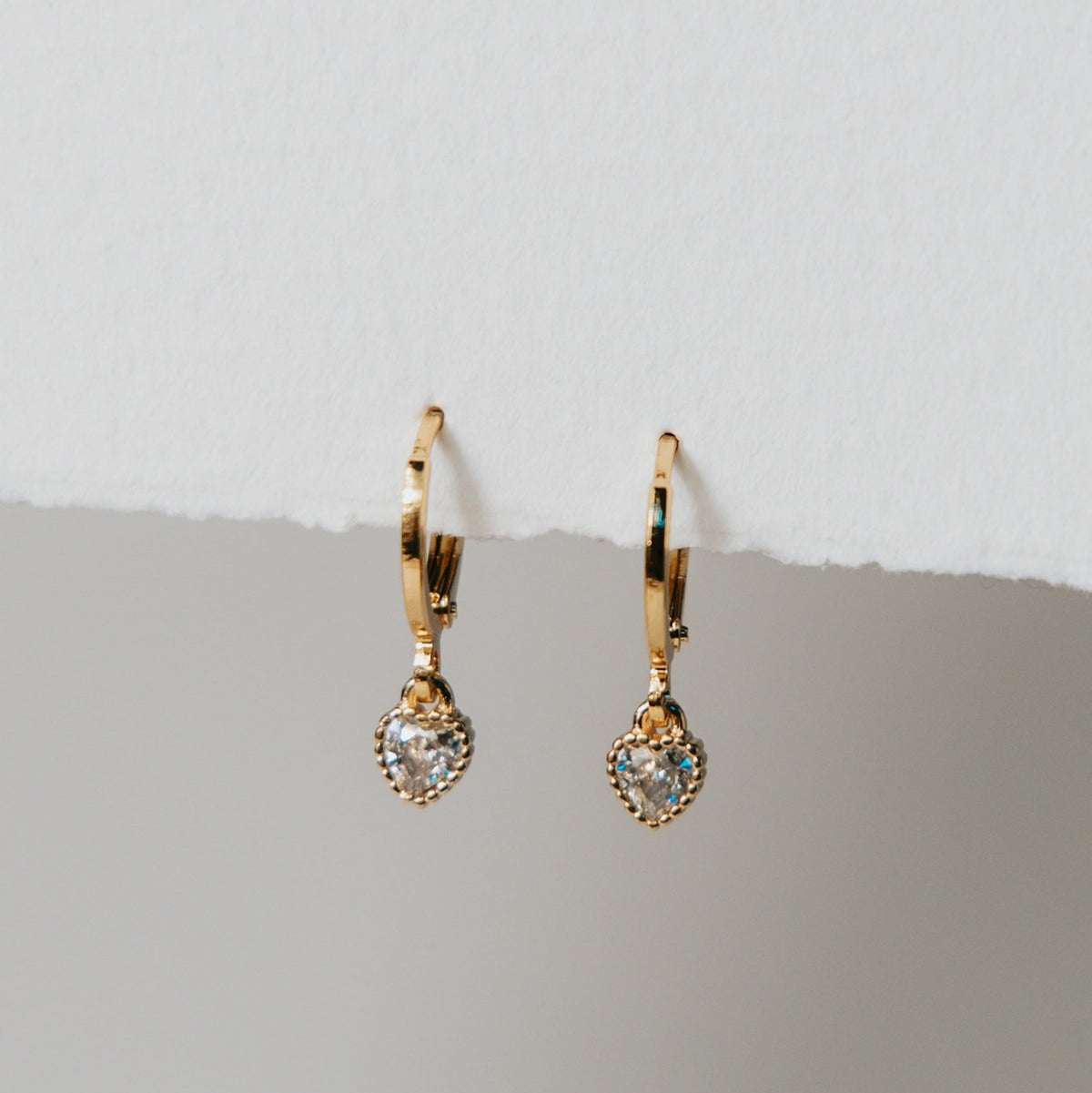 Rachel gold hoop earrings with tiny cubic zirconia hearts on a light grey background
