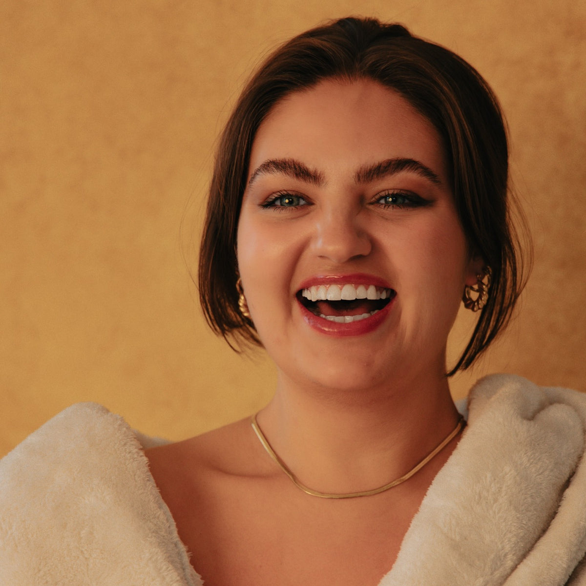 Woman laughing in a cream robe, wearing the Sienna gold herringbone chain necklace