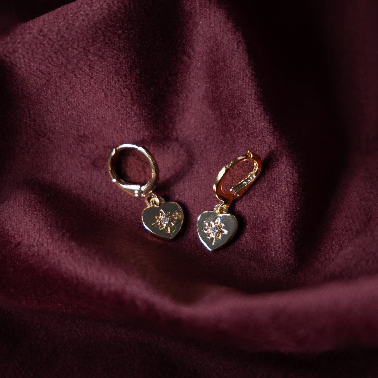 Heart-shaped gold hoop earrings on a burgundy fabric background
